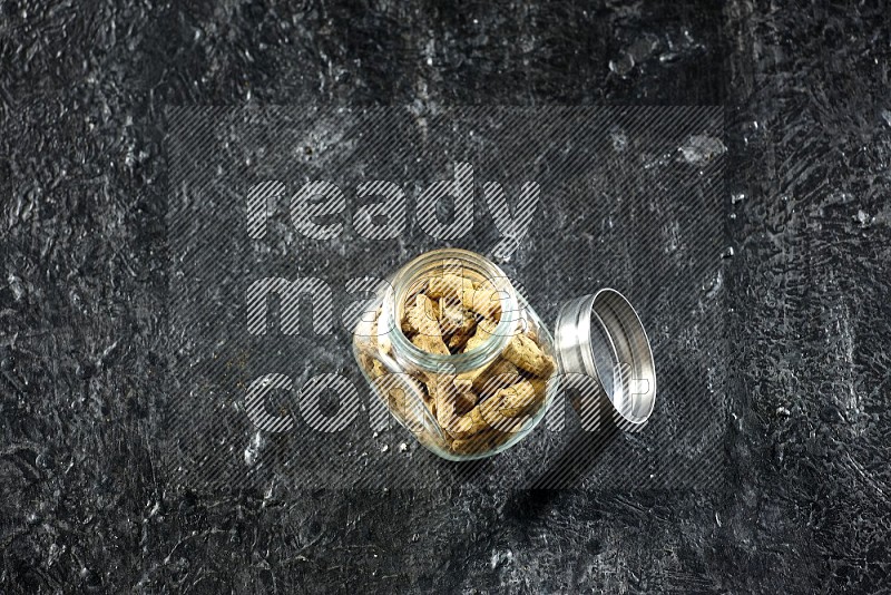 A glass spice jar full of dried turmeric whole fingers on a textured black flooring