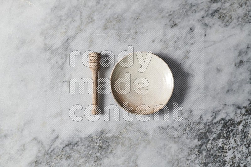 Beige Pottery Plate with wooden honey handle on the side on grey marble flooring, Top view