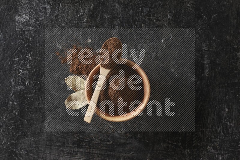 وعاء خشبي وملعقة خشبية ممتلئان ببودرة القرنفل مع أوراق الغار على خلفية سوداء