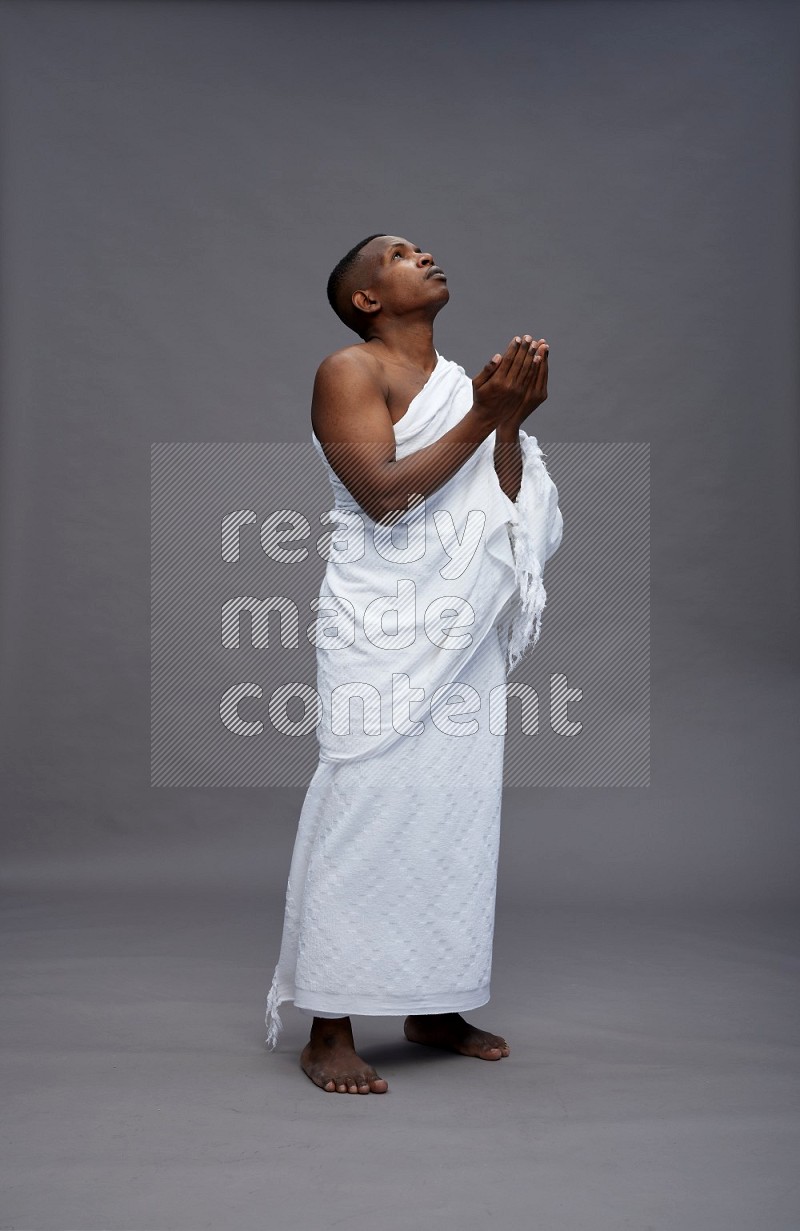 A man wearing Ehram Standing dua'a on gray background