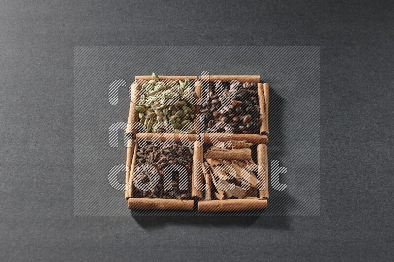 4 squares of cinnamon sticks full of coffee beans, cinnamon, cloves and cardamom on black flooring
