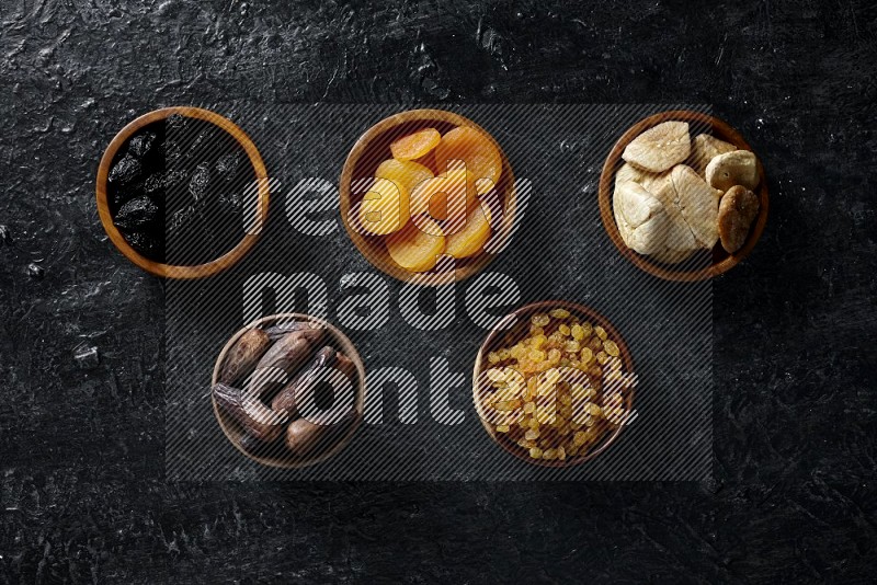 Dried fruits in wooden bowls in a dark setup