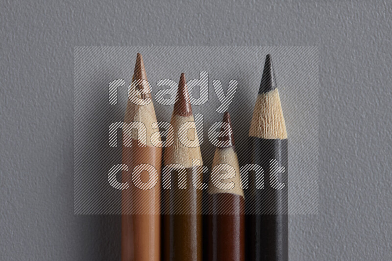 A collection of colored pencils arranged showcasing a gradient of brown hues on grey background