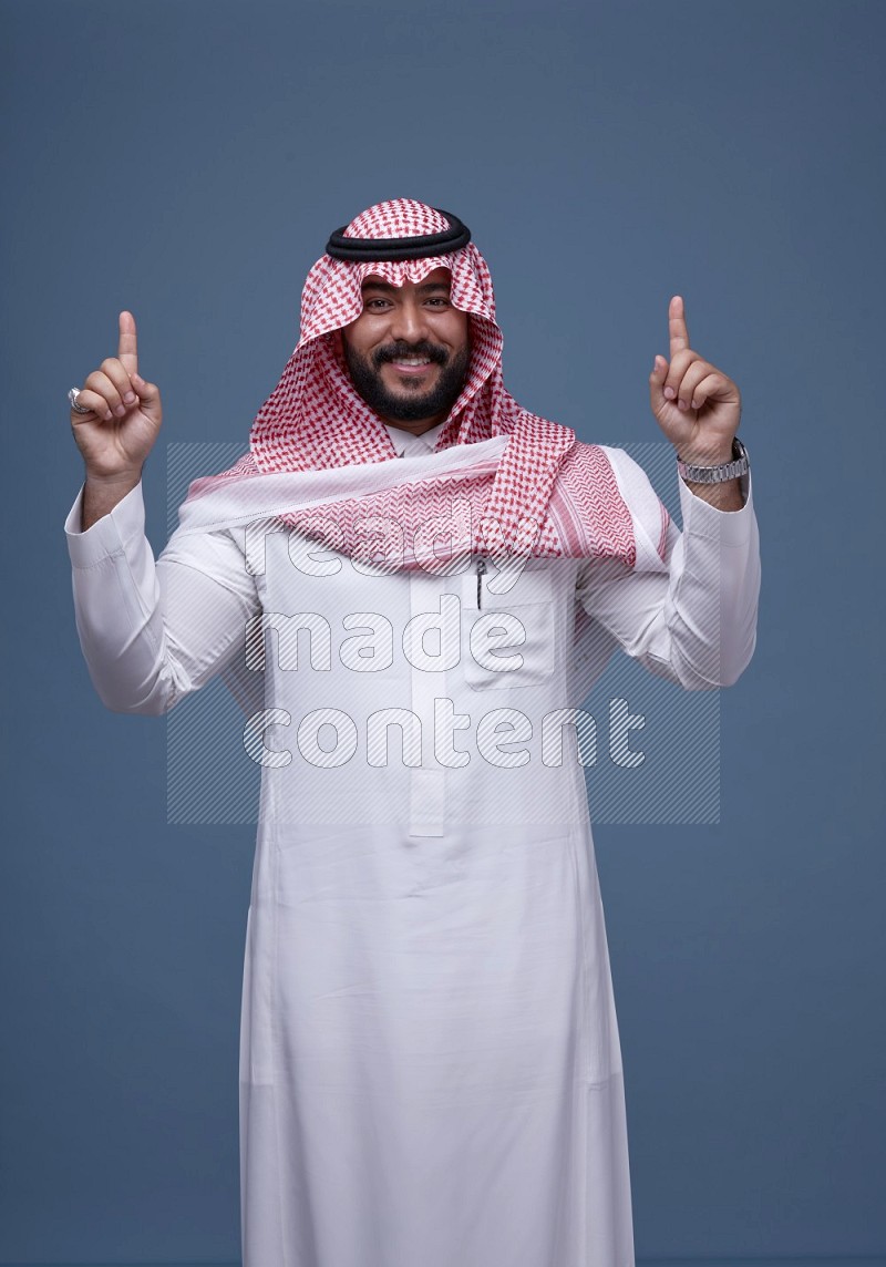 A Saudi man posing on blue background wearing Thob and Shomag