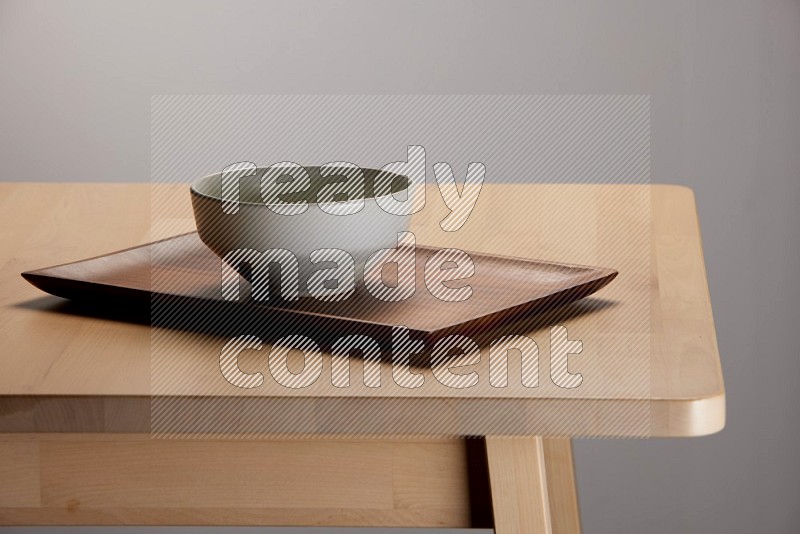 grey bowl placed on a rectangular wooden tray on the edge of wooden table