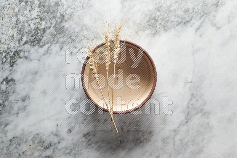 Wheat stalks on Beige Pottery Oven Bowl Plate on grey marble flooring, Top view
