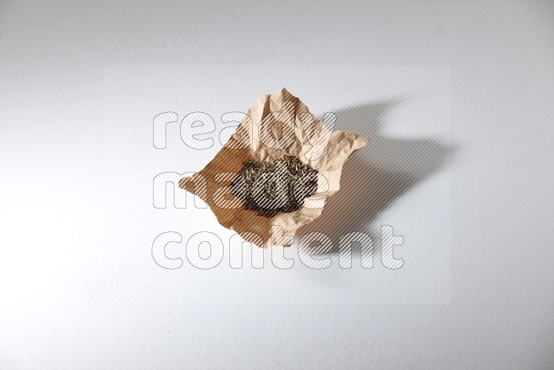 Cumin seeds in a crumpled piece of paper on white flooring