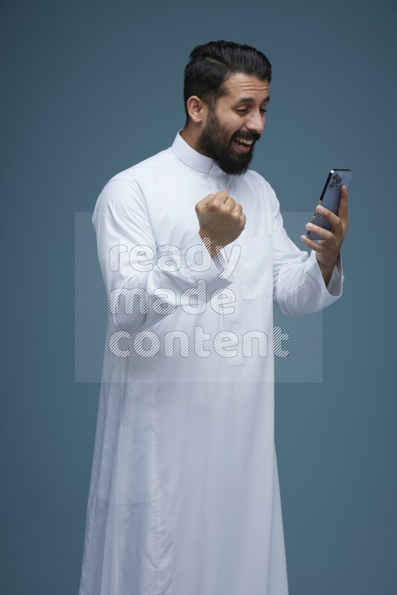 A man Texting in a blue background wearing Saudi Thob