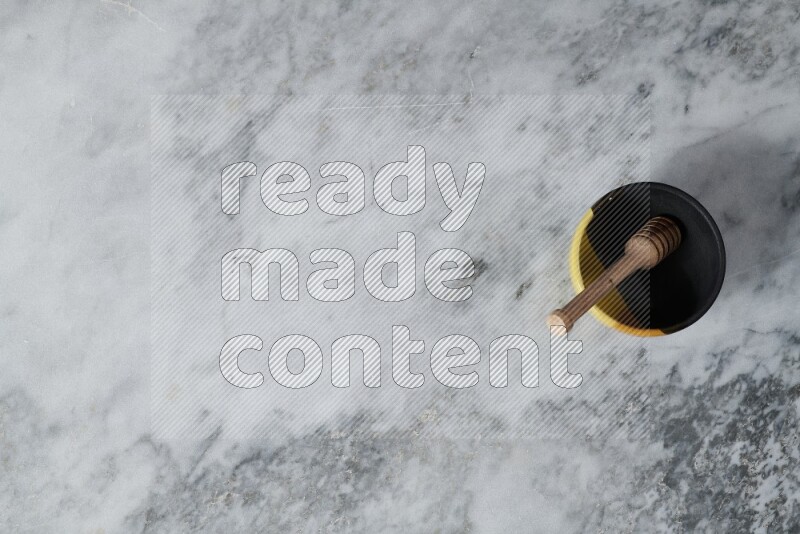 Multicolored pottery bowl with wooden honey dipper in it on grey marble background