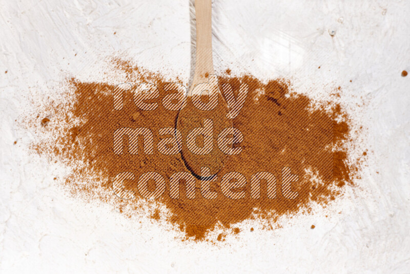 A wooden spoon full of ground paprika powder and surrounded with the powder on white background