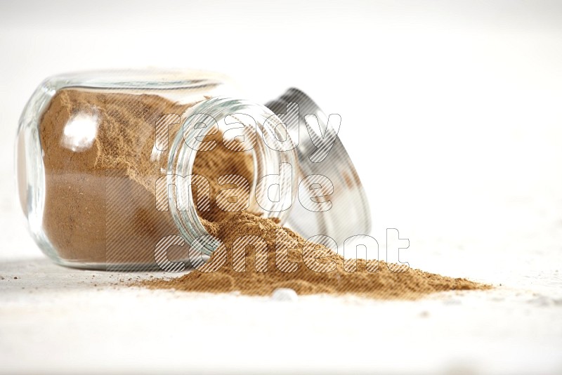 Flipped glass jar full of cinnamon powder on a textured white background