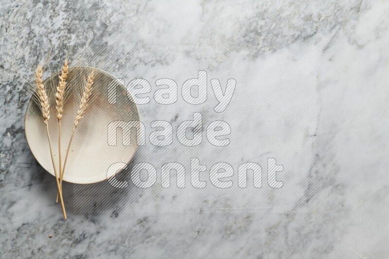 Wheat stalks on multicolored pottery plate on grey marble background