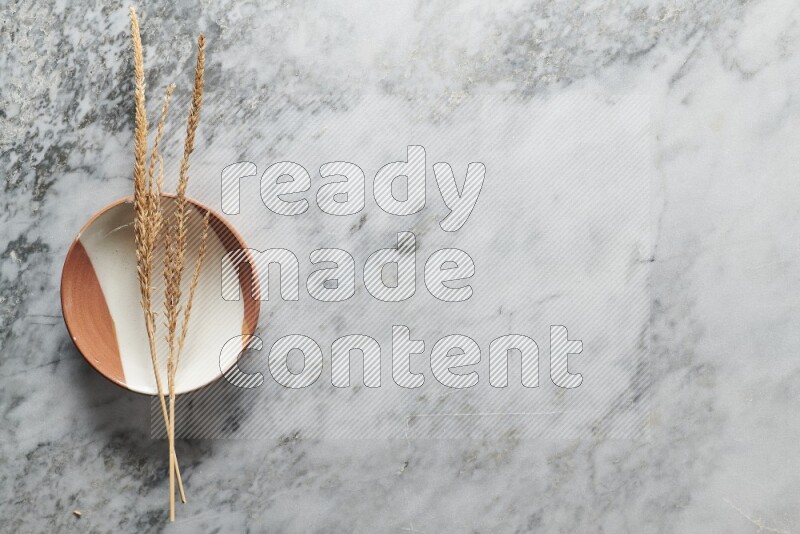 Wheat stalks on multicolored pottery plate on grey marble background