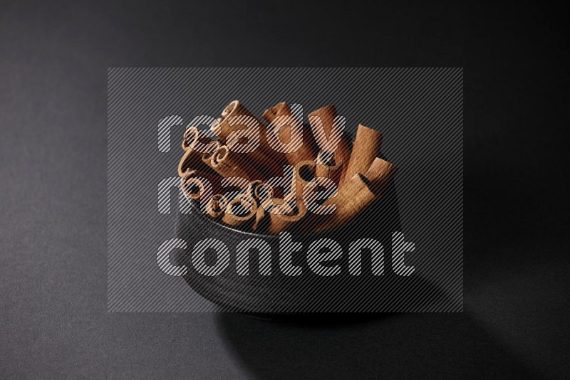 Cinnamon sticks in a black bowl on a black background in different angles