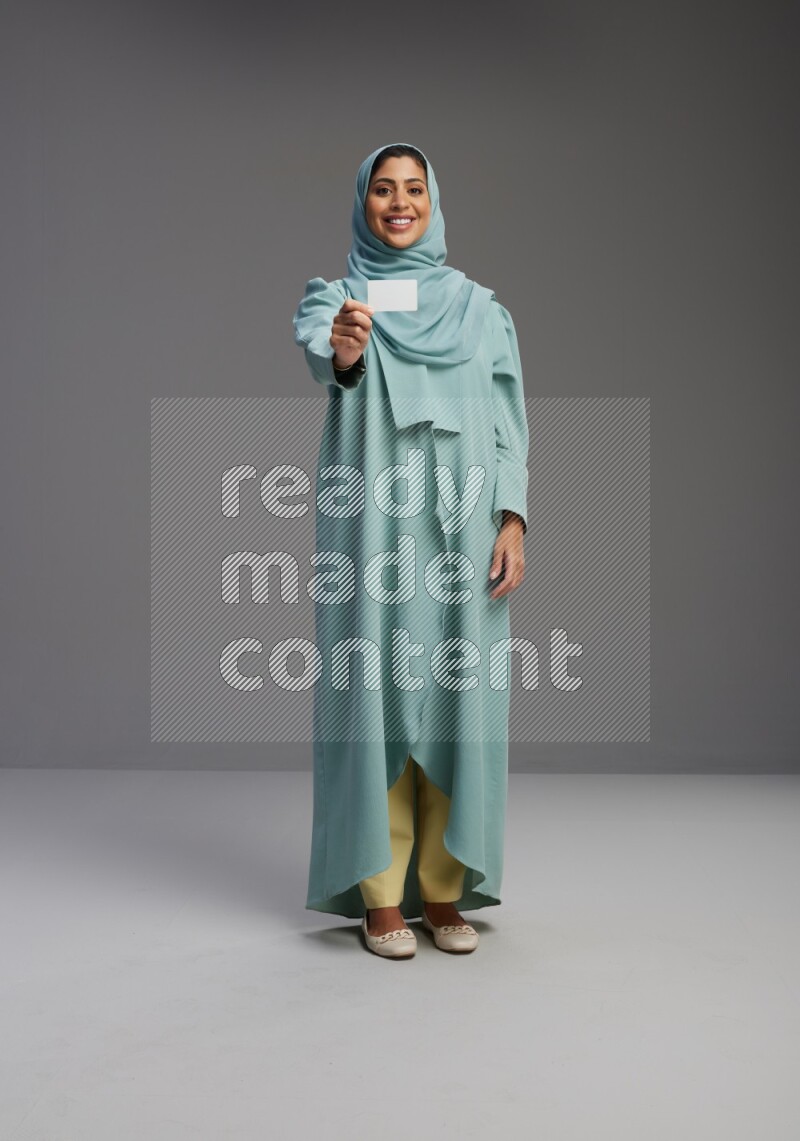 Saudi Woman wearing Abaya standing holding ATM card on Gray background