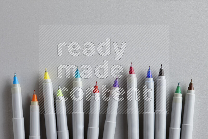 An arrangement of open coloring pens in different colors without the caps on grey background