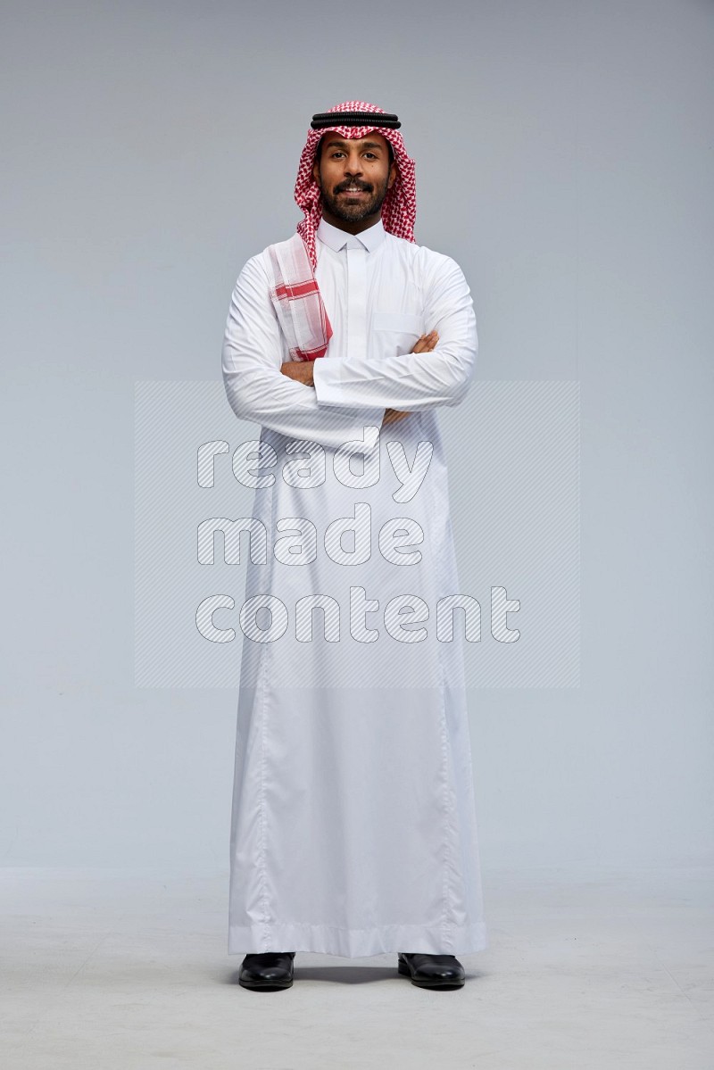 Saudi man Wearing Thob and shomag standing with crossed arms on Gray background