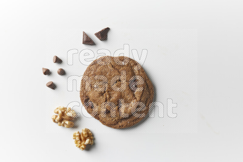 A single chocolate chips cookie with chocolate and walnuts beside it on a white background