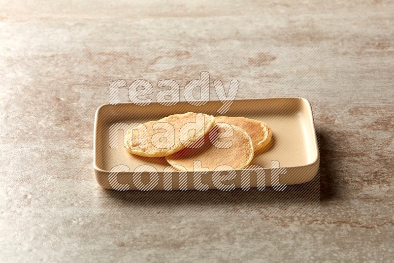 Three stacked plain mini pancakes in a rectangular plate on beige background