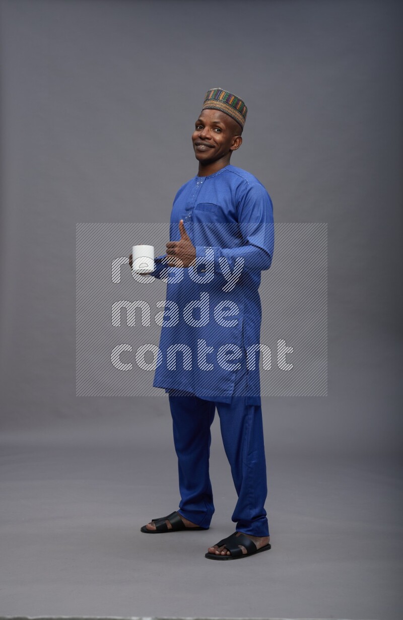 Man wearing Nigerian outfit standing holding mug on gray background