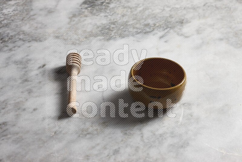 Multicolored pottery bowl with wooden honey dipper on the side on grey marble background