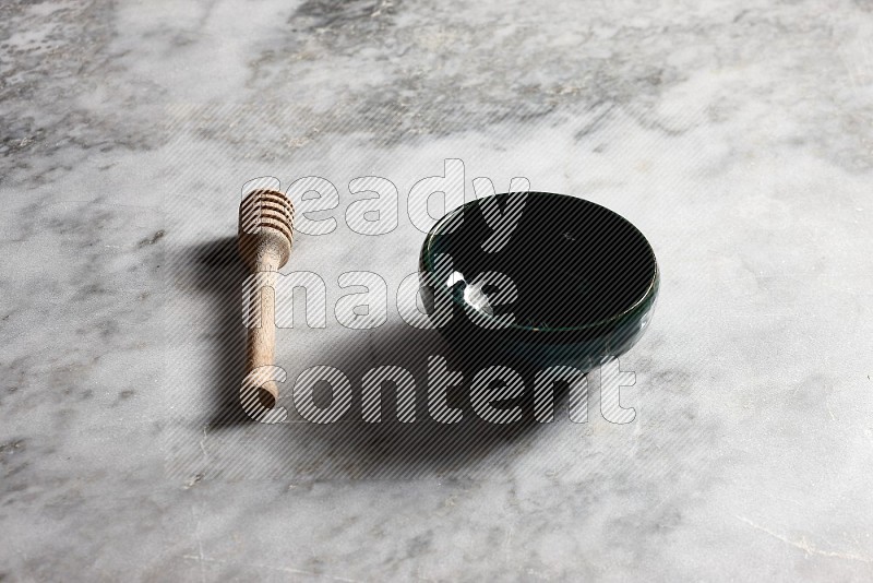 Dark Green Pottery bowl with wooden honey handle on the side with grey marble flooring, 45 degree angle