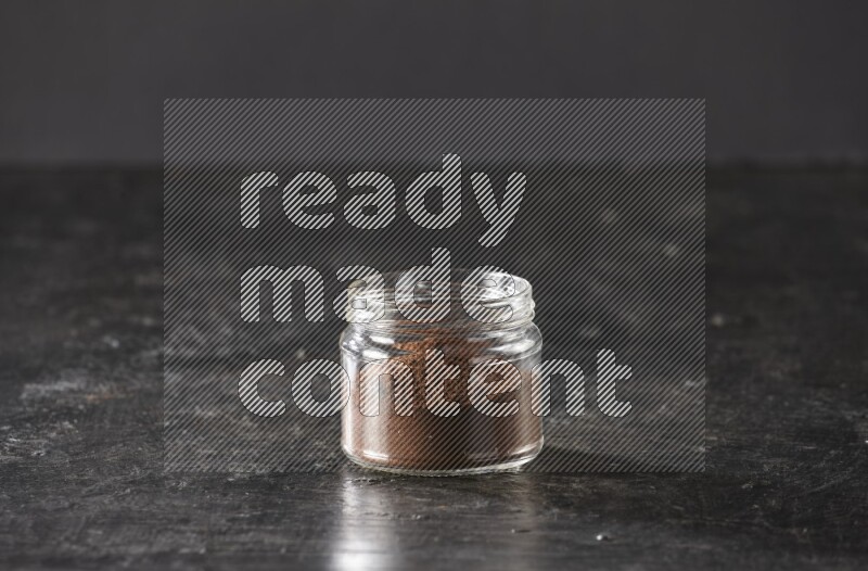 A glass jar full of cloves powder on a textured black flooring