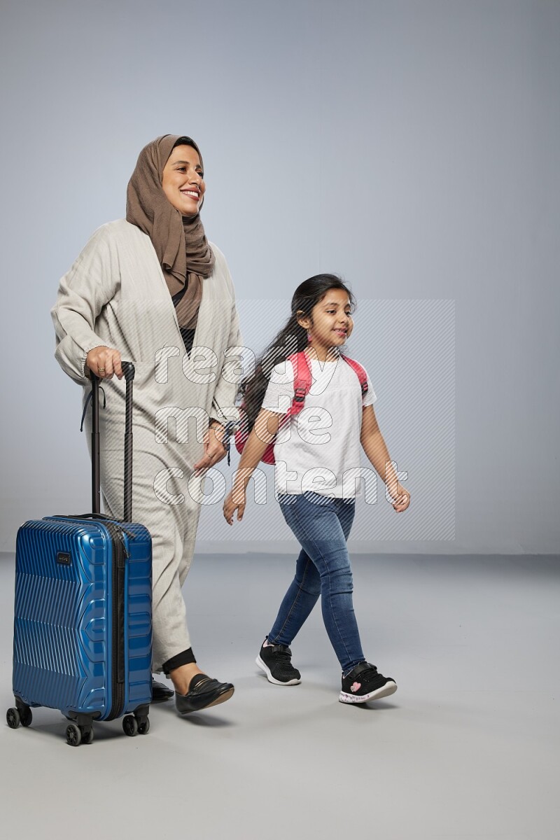 Mom and daughter standing pulling a carry-on bag on gray background