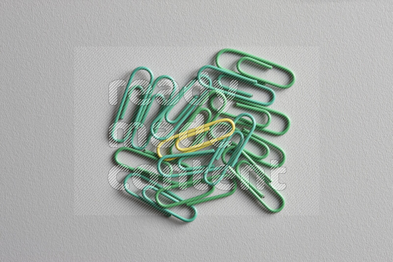 A bunch of green paper clips with a different colored paper clip in the center on grey background