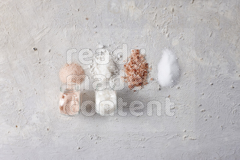 4 glass jars filled with table salt, coarse sea salt, fine himalayan salt and coarse himalayan salt on white background