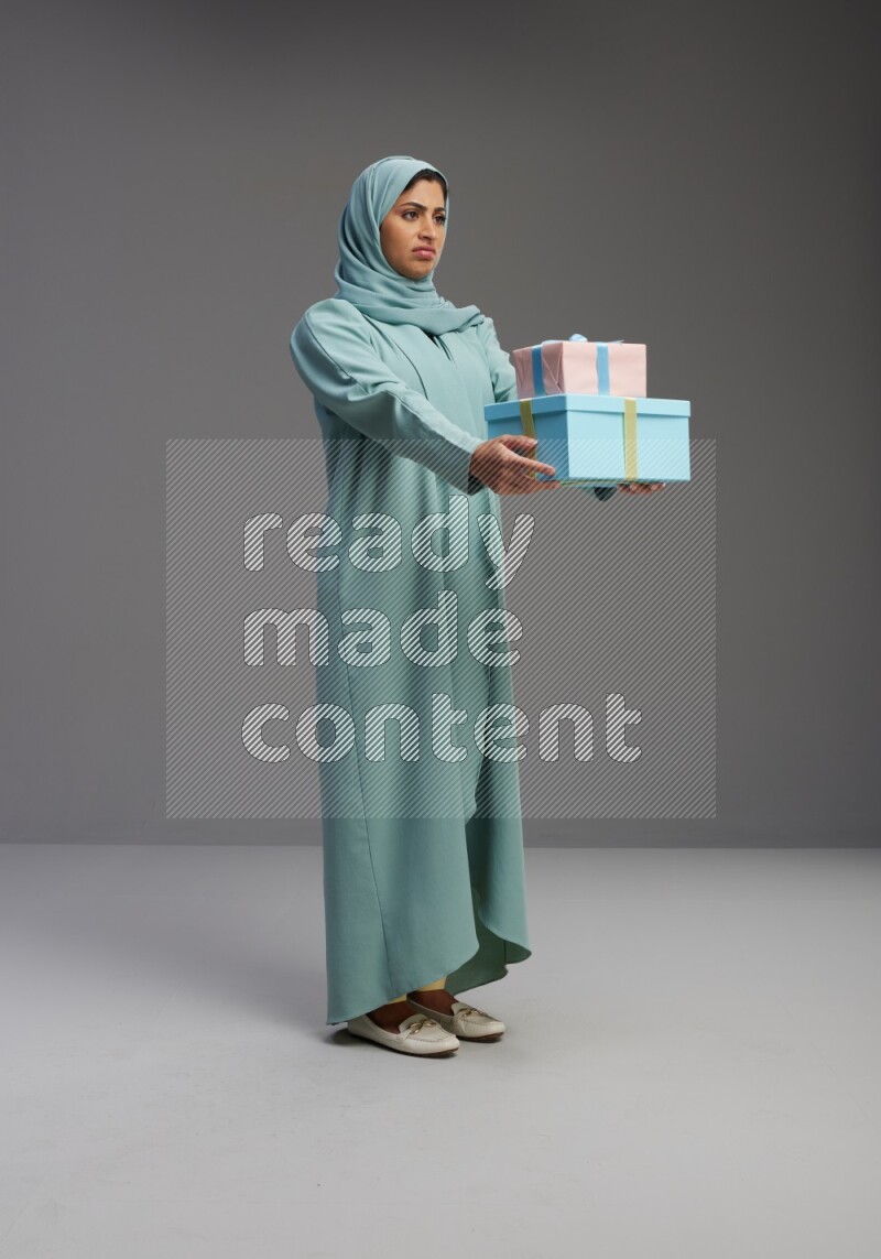 Saudi Woman wearing Abaya standing holding gift box on Gray background
