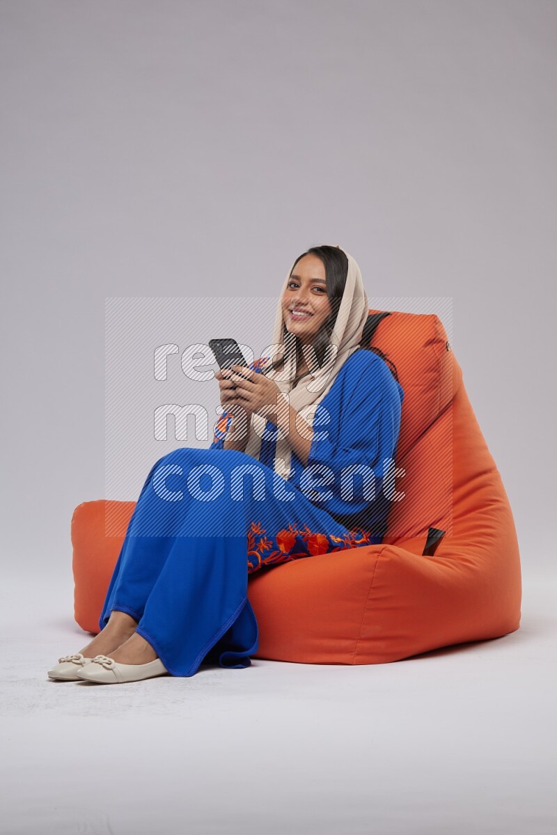 A Saudi woman sitting on an orange beanbag and texting on phone