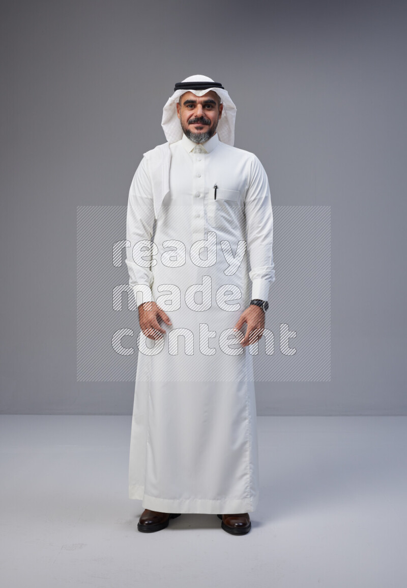 Saudi man Wearing Thob and white Shomag standing interacting with the camera on Gray background