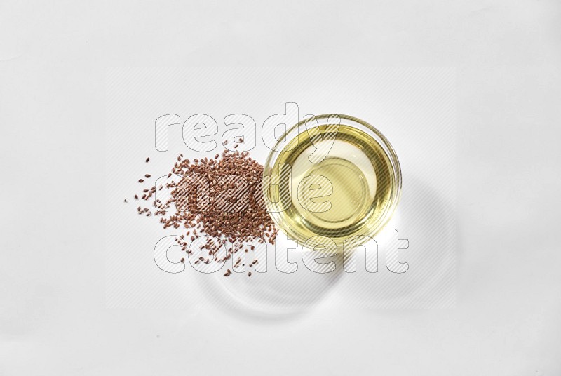A glass bowl full of flaxseeds oil and flaxseeds beside it on a white flooring