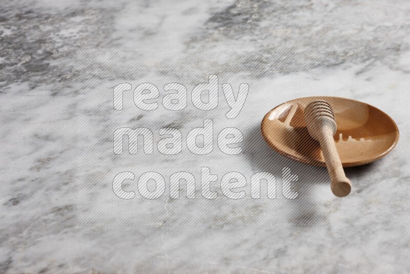 Multicolored pottery plate with wooden honey dipper in it on grey marble background