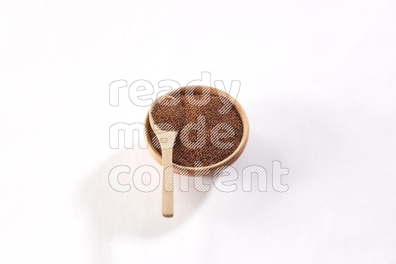 A wooden bowl and spoon full of garden cress seeds on a white flooring