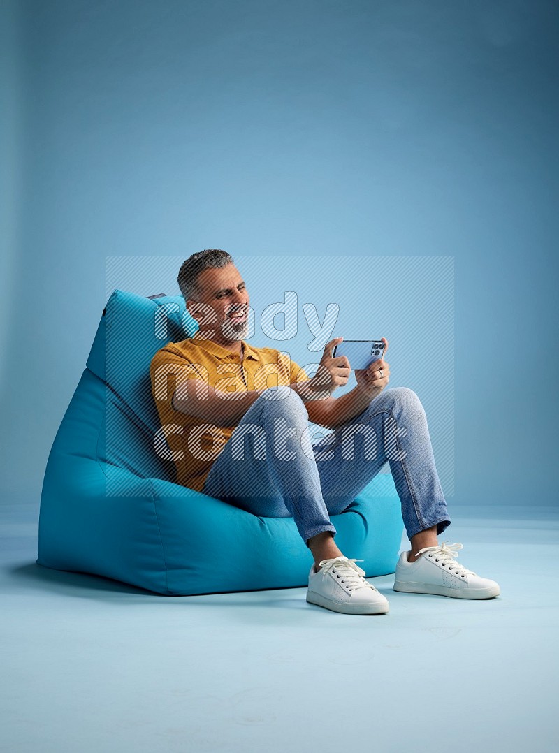 A man sitting on a blue beanbag and playing on phone