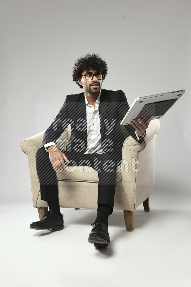 A man wearing formal sitting on a chair holding a laptop on white background