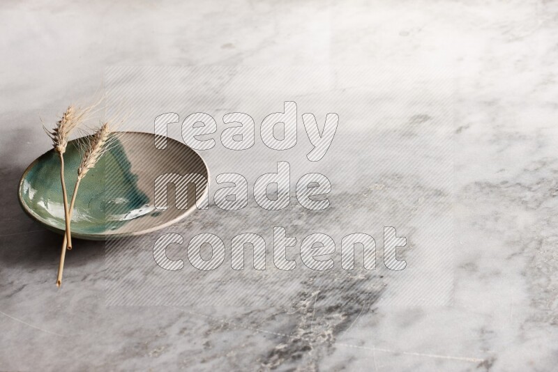 Wheat stalks on multicolored pottery plate on grey marble background