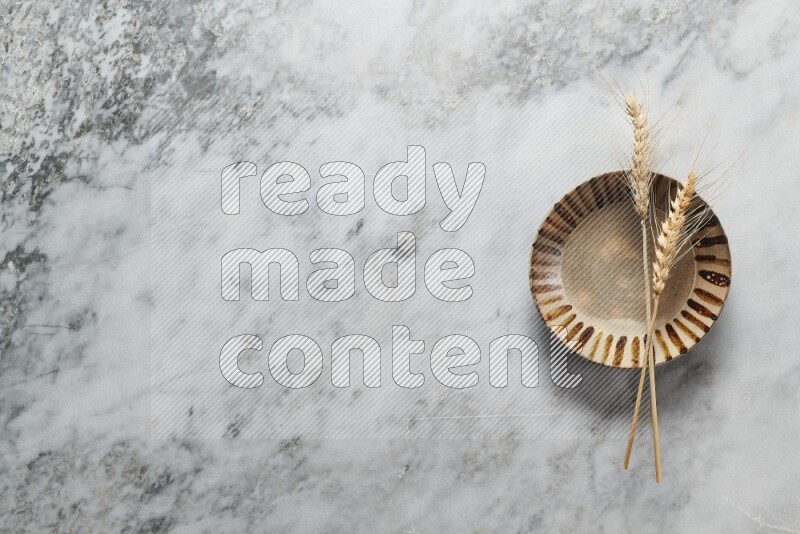 Wheat stalks on multicolored pottery plate on grey marble background