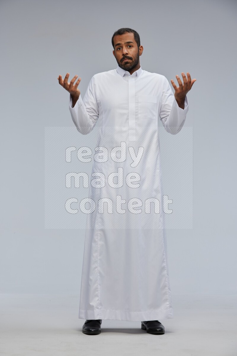 Saudi man Wearing Thob standing interacting with the camera on Gray background