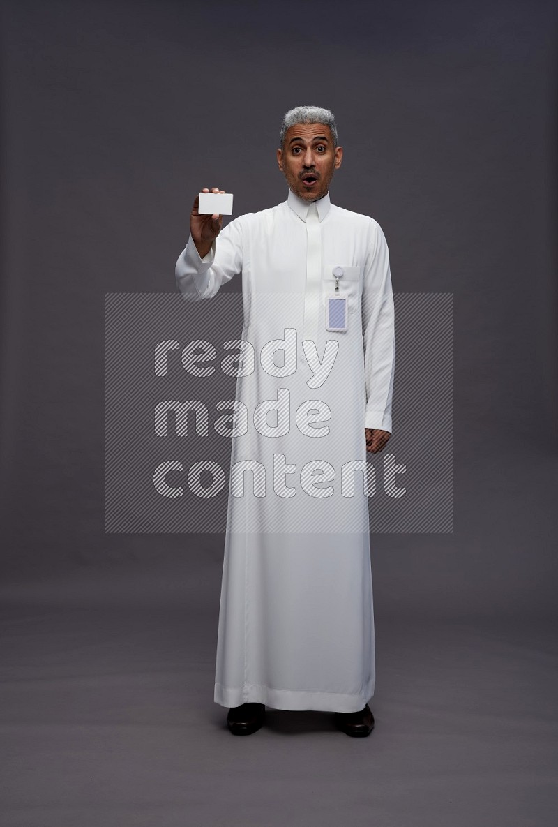 Saudi man wearing thob with pocket employee badge standing holding ATM card on gray background