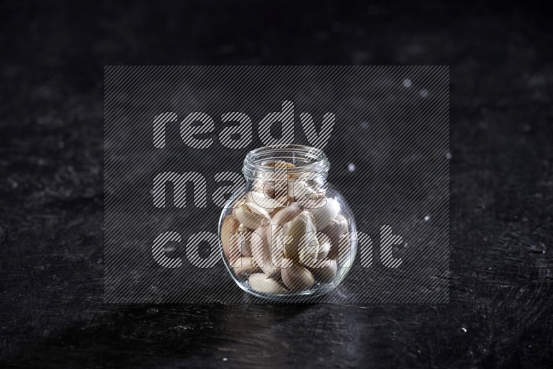 A glass spice jar full of garlic cloves on a textured black flooring in different angles