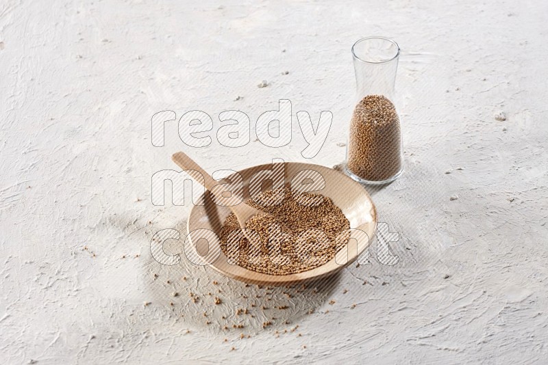 A multicolored pottery plate and a wooden spoon and a glass jar filled with mustard seeds on a textured white flooring in different angles