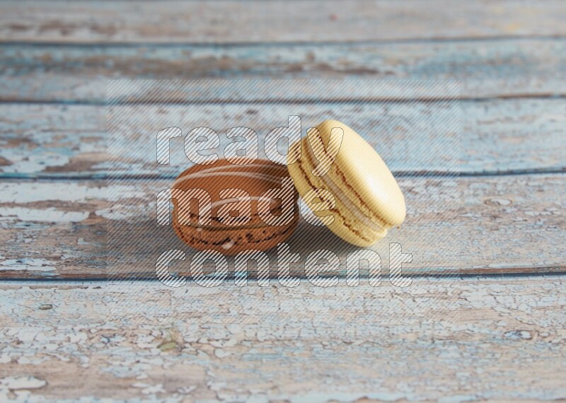 45º Shot of of two assorted Brown Irish Cream, and Yellow Vanilla macarons on light blue background