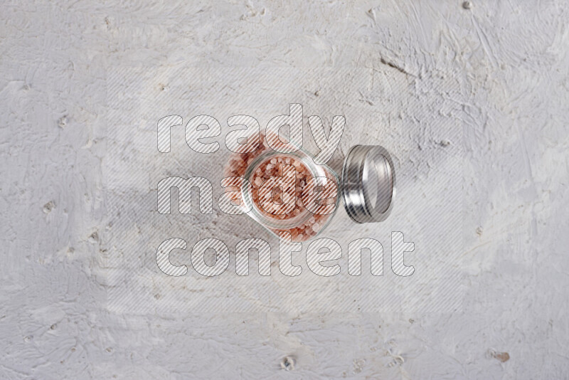 A glass jar full of coarse himalayan salt crystals on white background