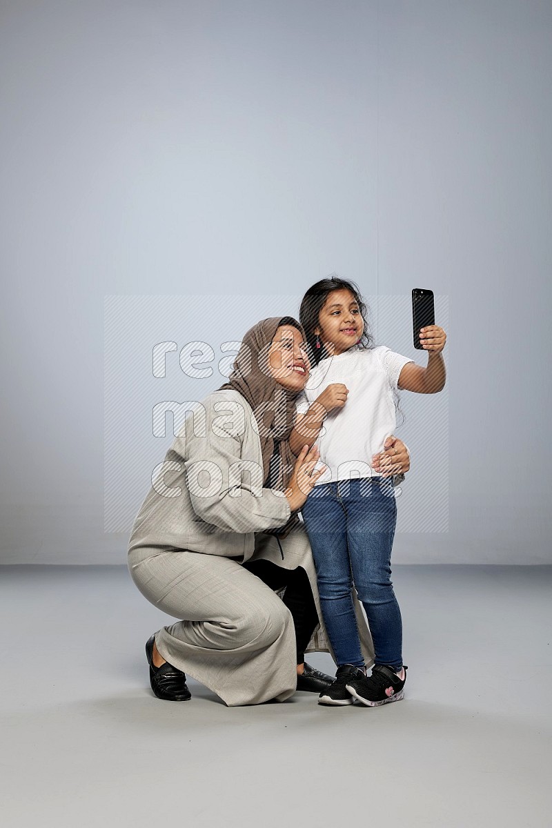 A girl standing taking selfie with her mother on gray background
