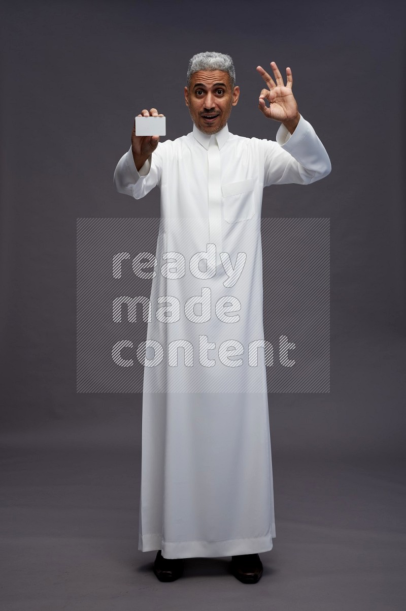 Saudi man wearing thob standing holding ATM card on gray background