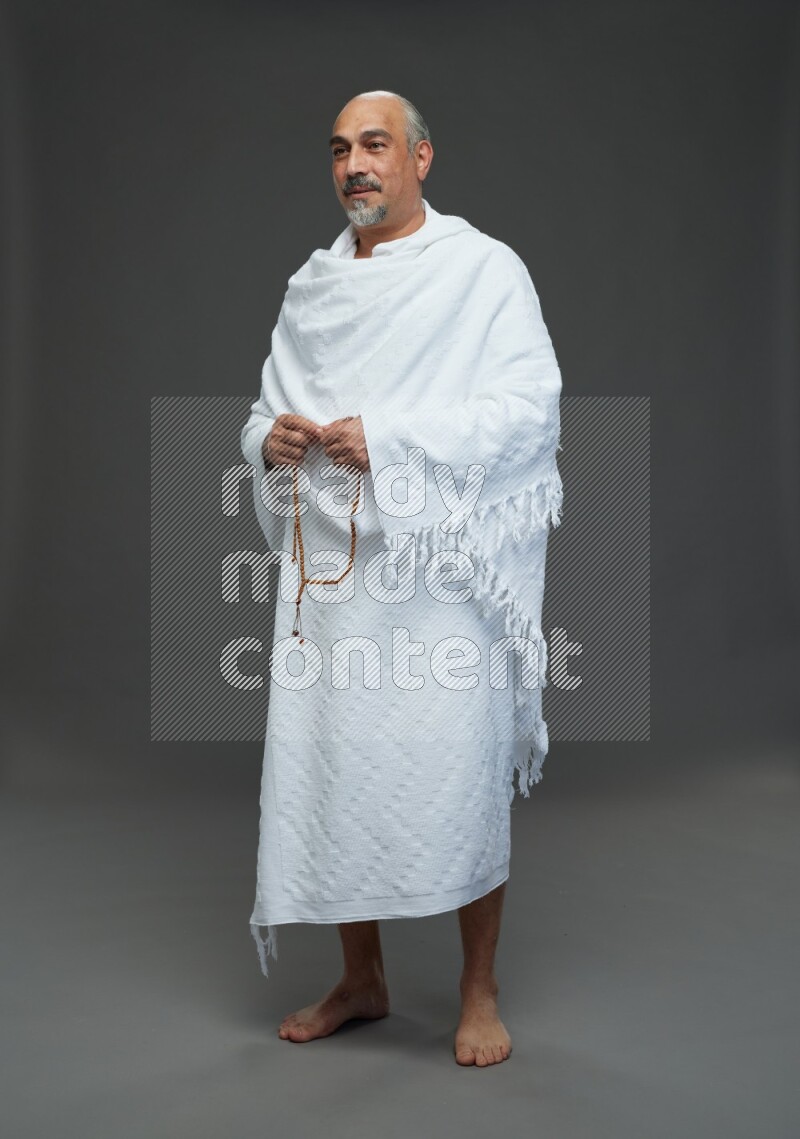 A man wearing Ehram Standing holding rosary on gray background