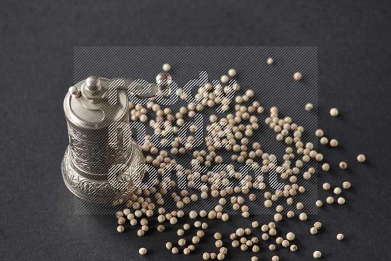 White pepper with a metal pepper grinder on black flooring
